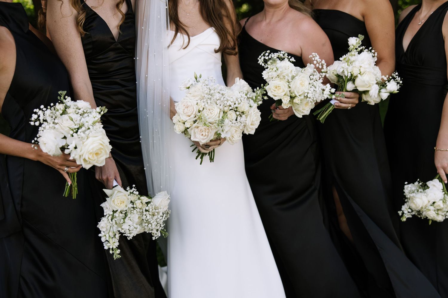 Wedding party holding white floral bouquets against black dresses.