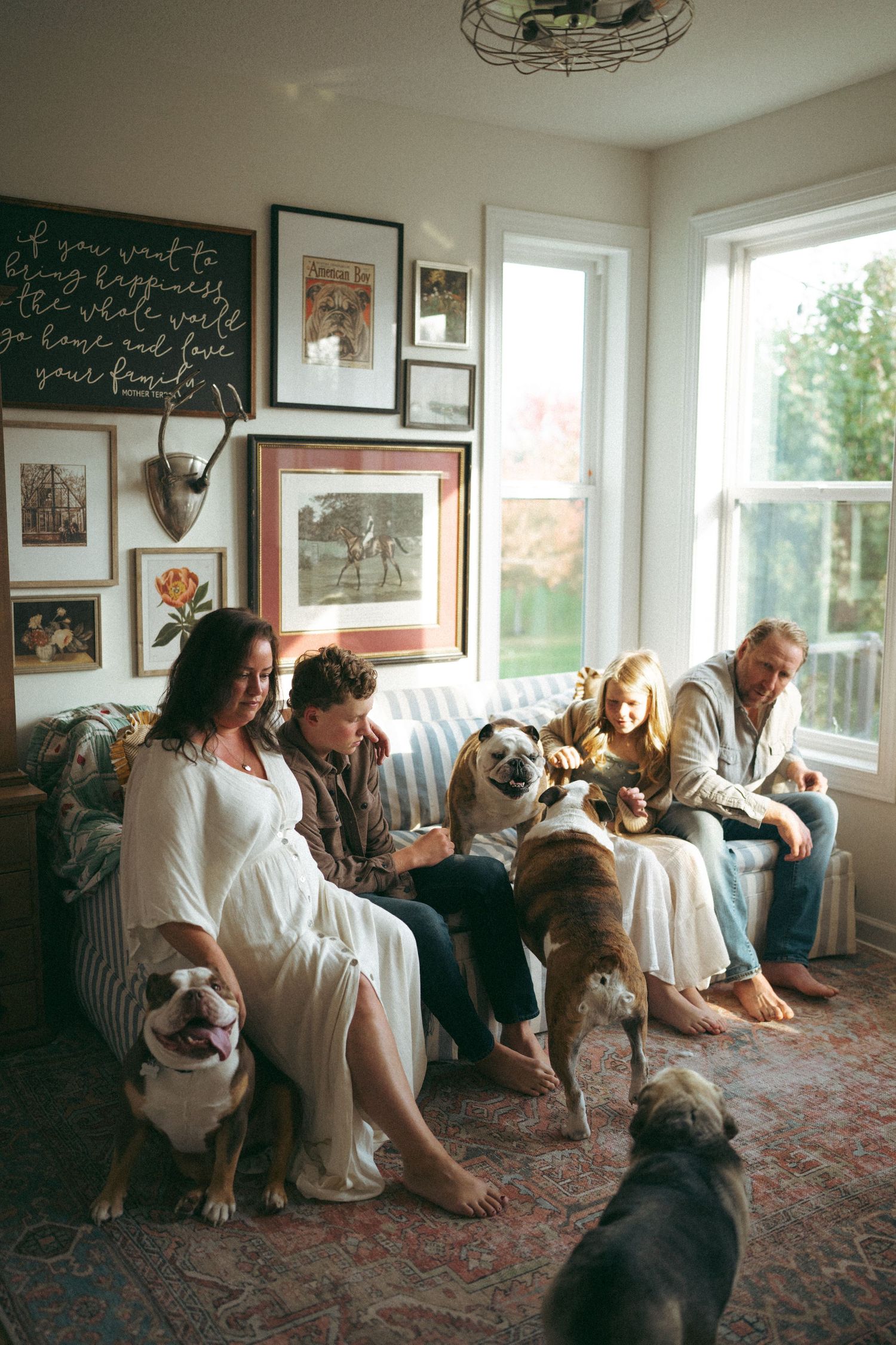 Family and dogs gather on a cozy couch in a living room decorated with wall art and chalkboard.