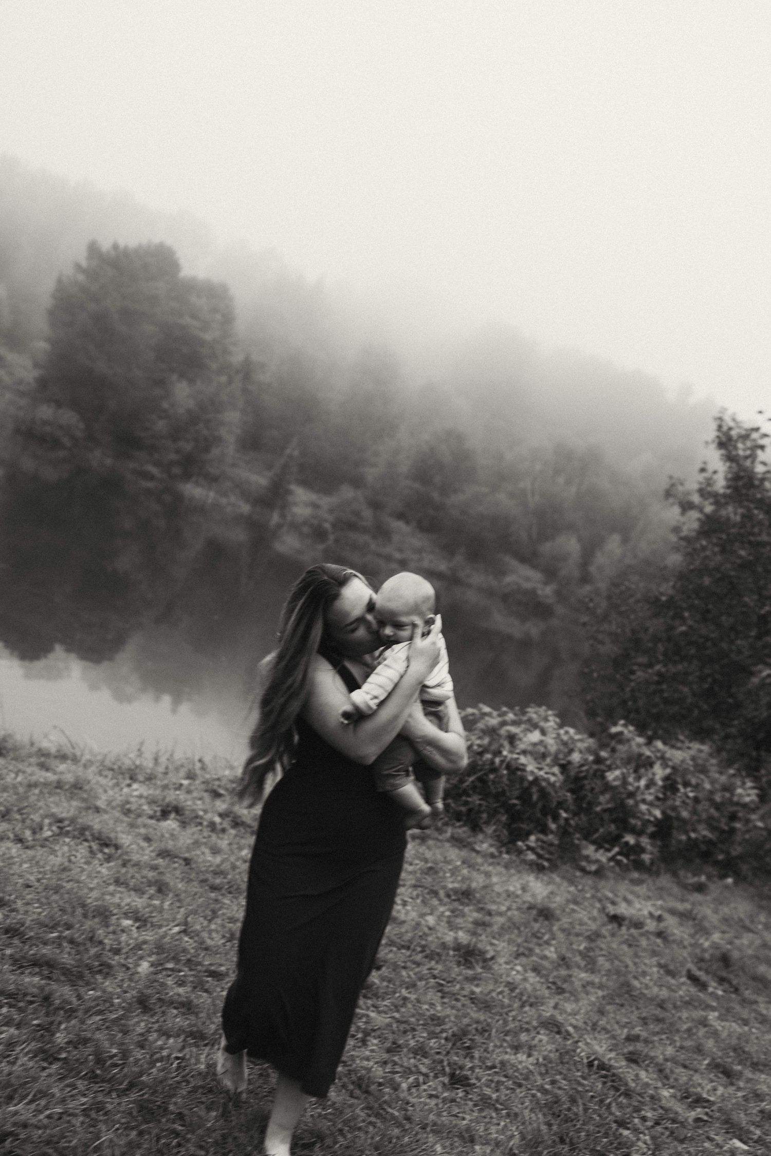 A misty lakeside scene with people sharing a tender moment against a forested backdrop.