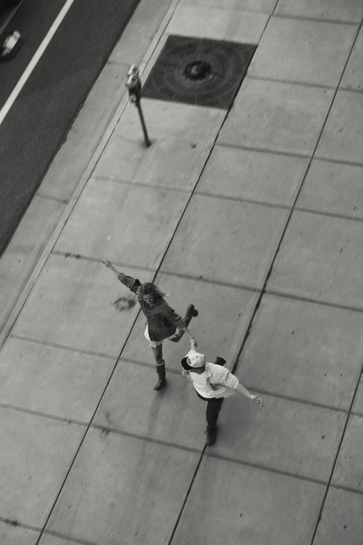 Aerial black and white view of two people walking on a tiled sidewalk.