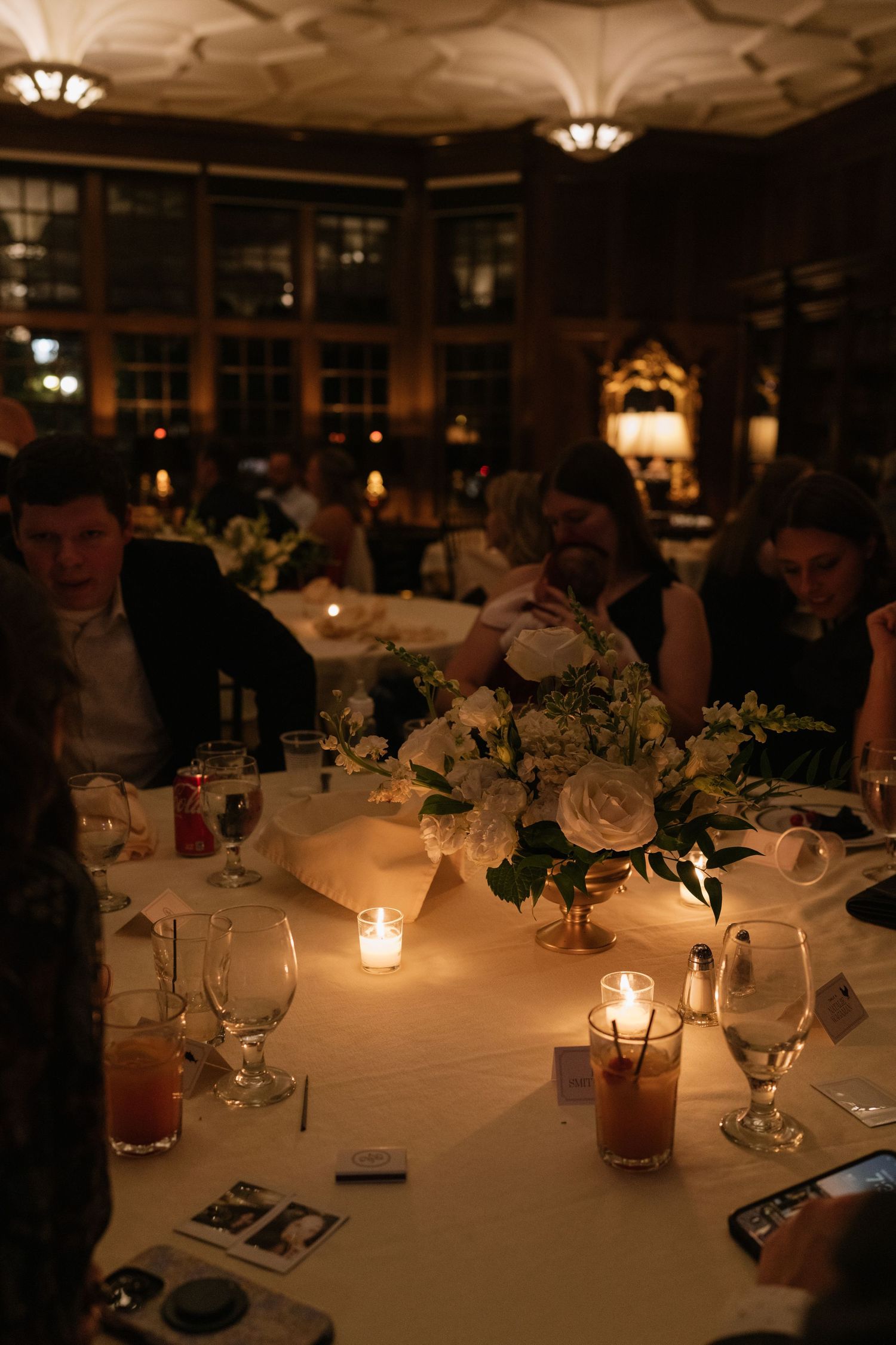 Elegant wedding reception tables set with white linens and candlelight in a dimly lit ballroom.