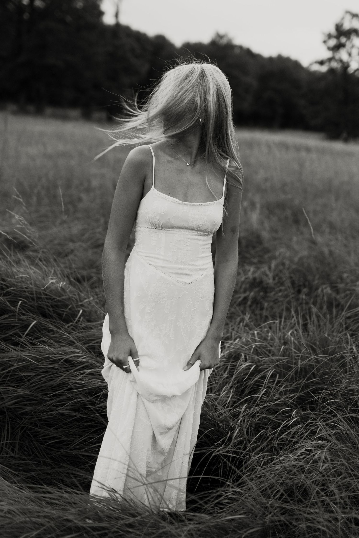 Black and white portrait in a field shows movement in a flowing white dress.