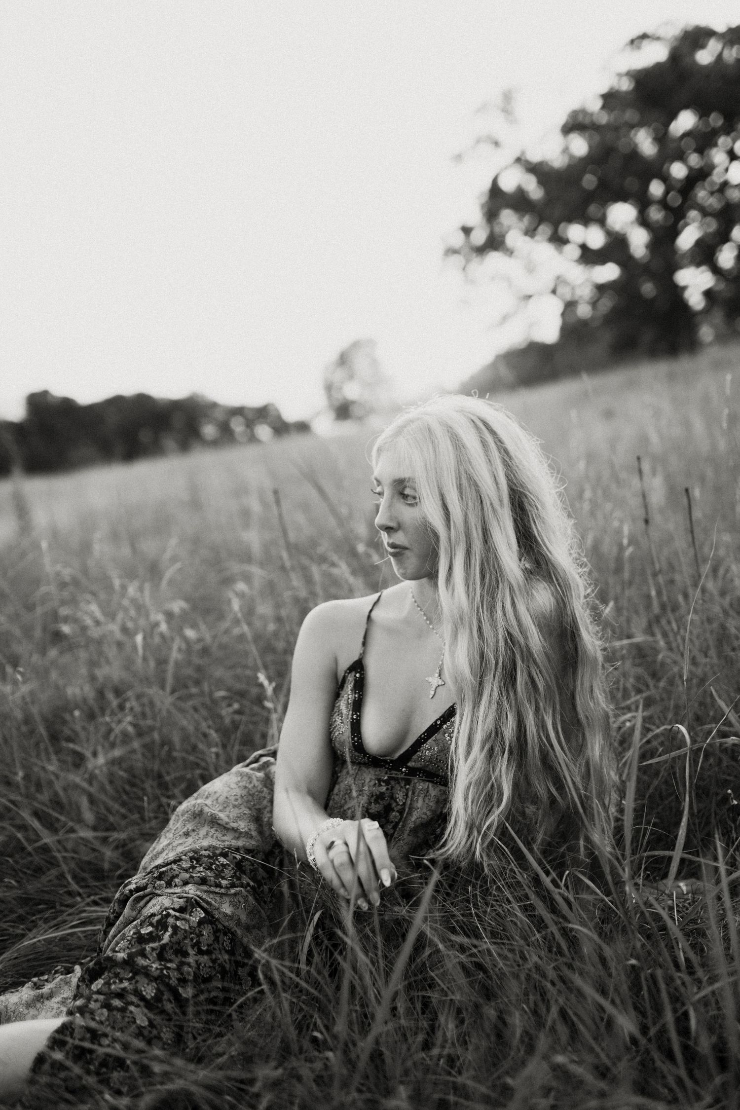 Black and white portrait of someone reclining in tall grass at sunset.