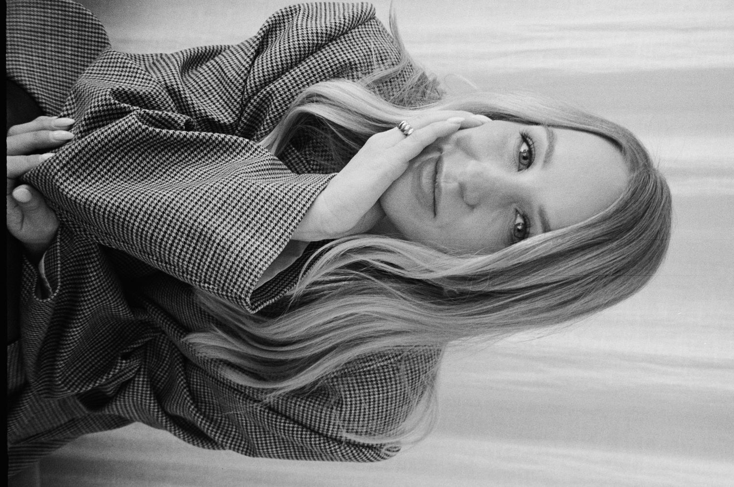 Black and white portrait of a woman with long blonde hair wearing a plaid shirt against a light background.