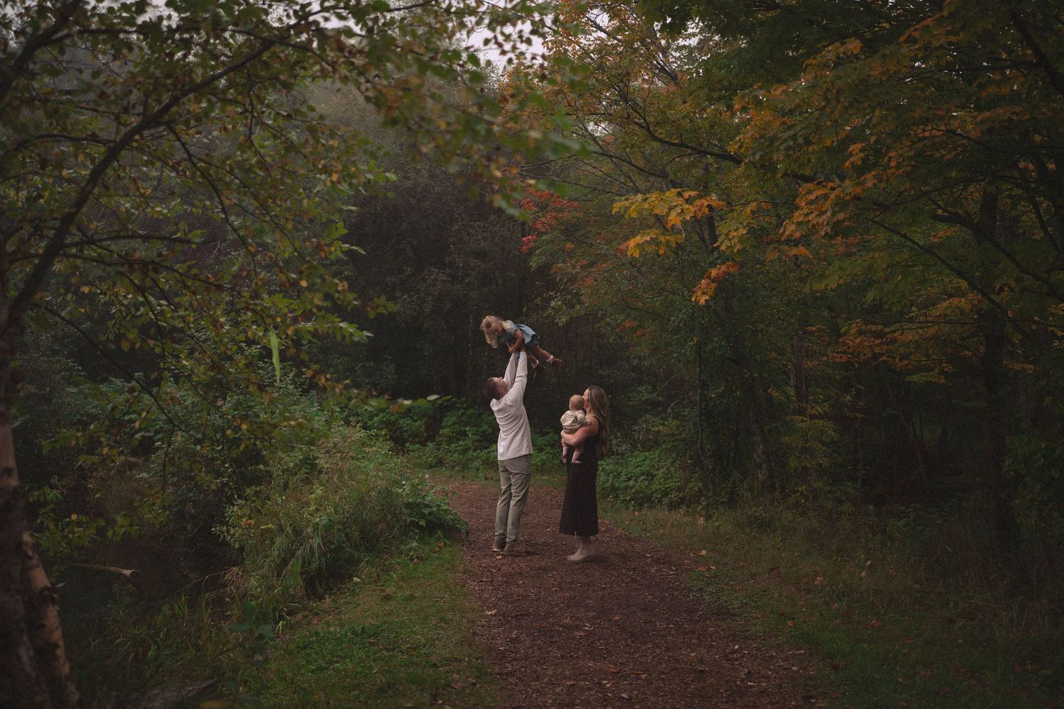 A wooded path through autumn trees with people walking in the distance.