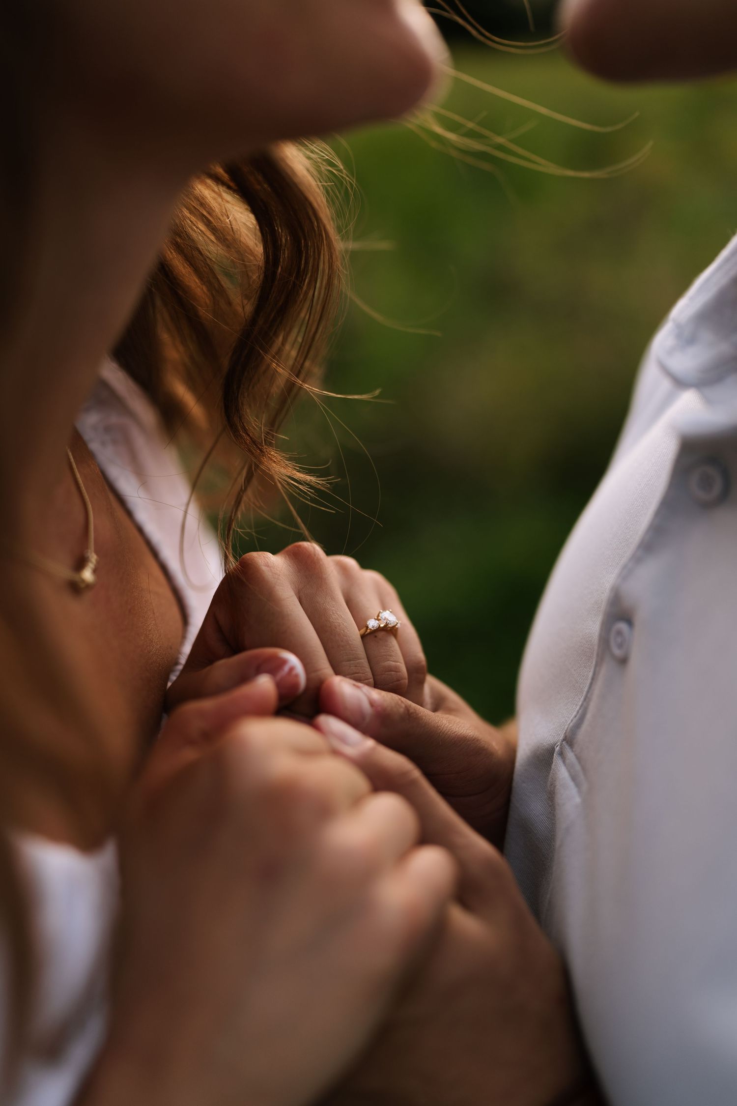Close-up shot of hands with an engagement ring in natural lighting.