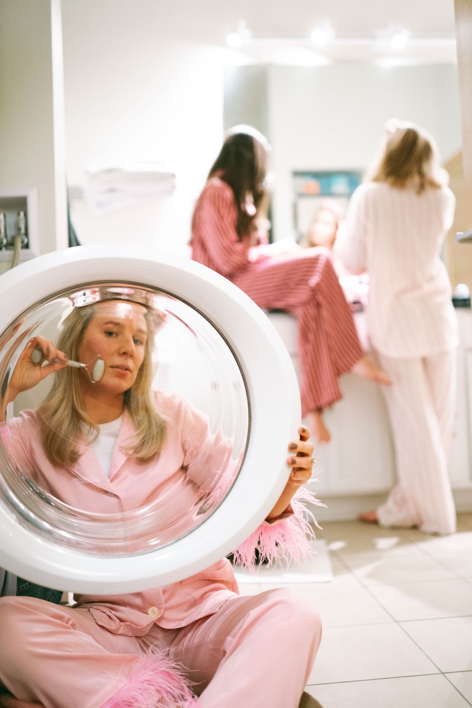 People in pink sleepwear having fun around a washing machine in a bright laundry room.
