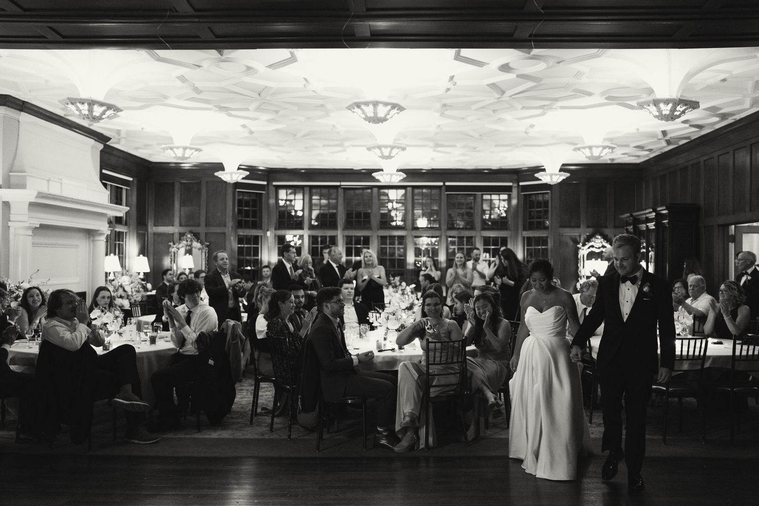 Black and white panoramic view of a wedding reception venue with guests mingling.
