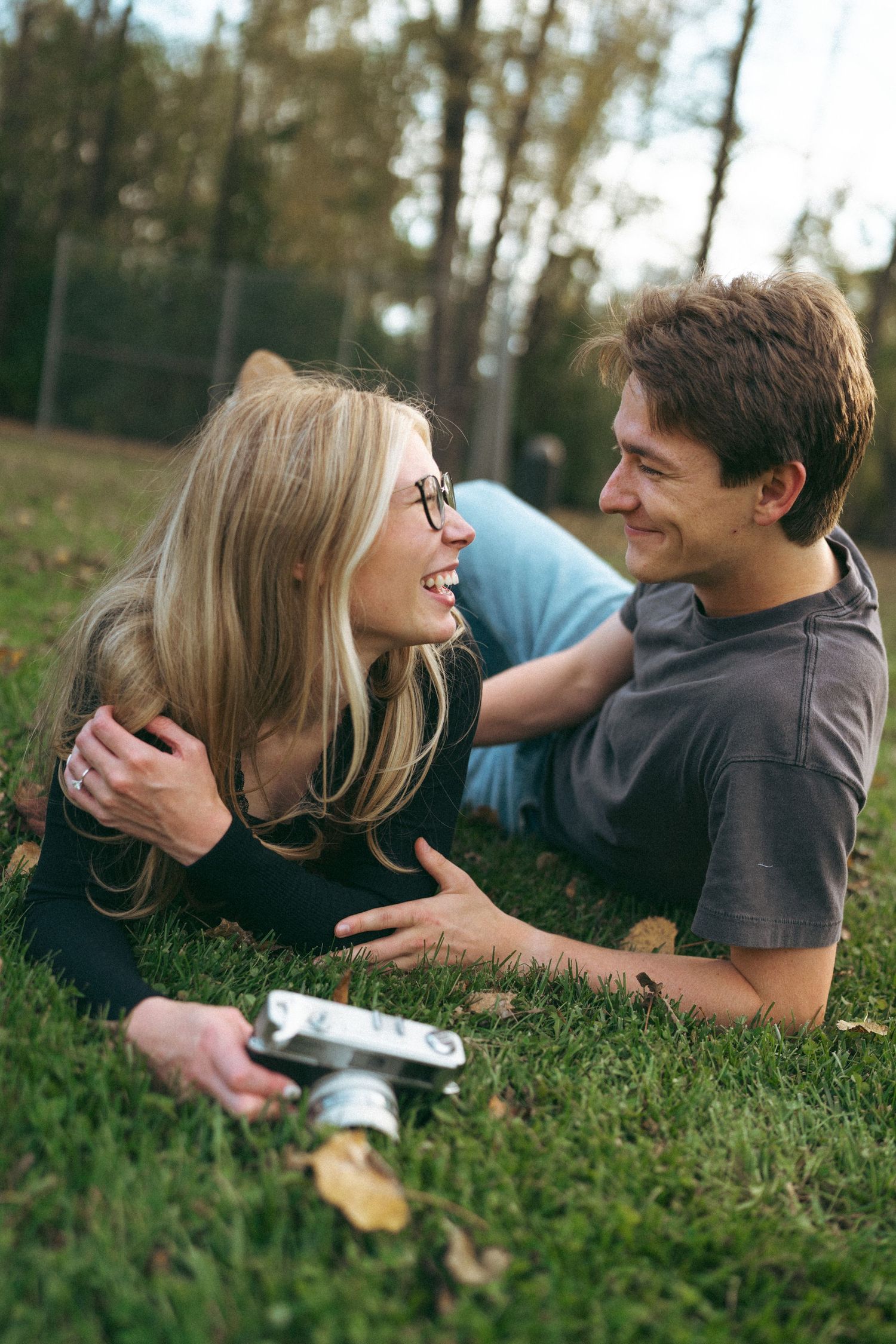 Couple lying in grass taking playful photos together outdoors.