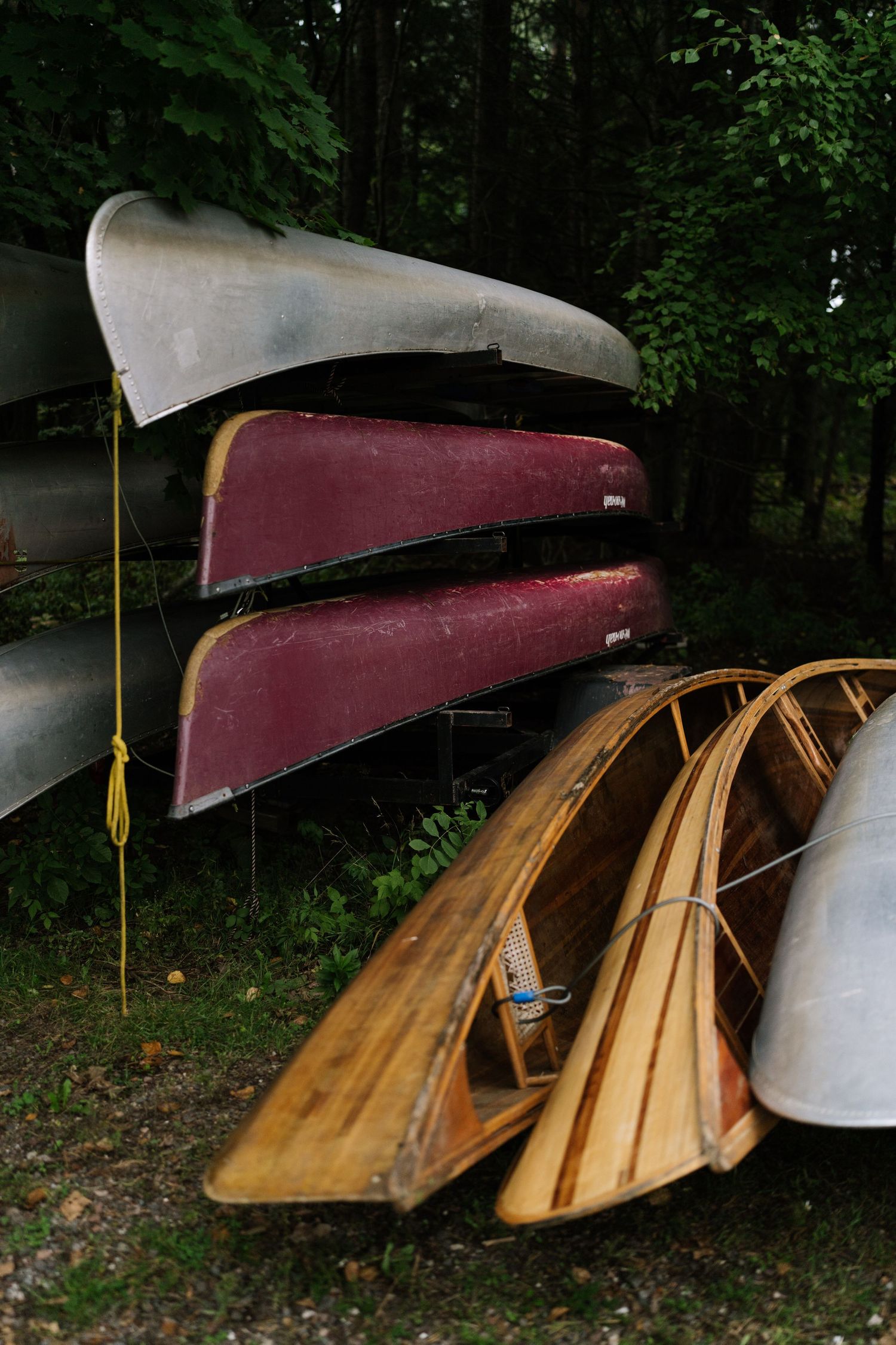 Wooden canoes lined up against trees with burgundy covers on their tops.