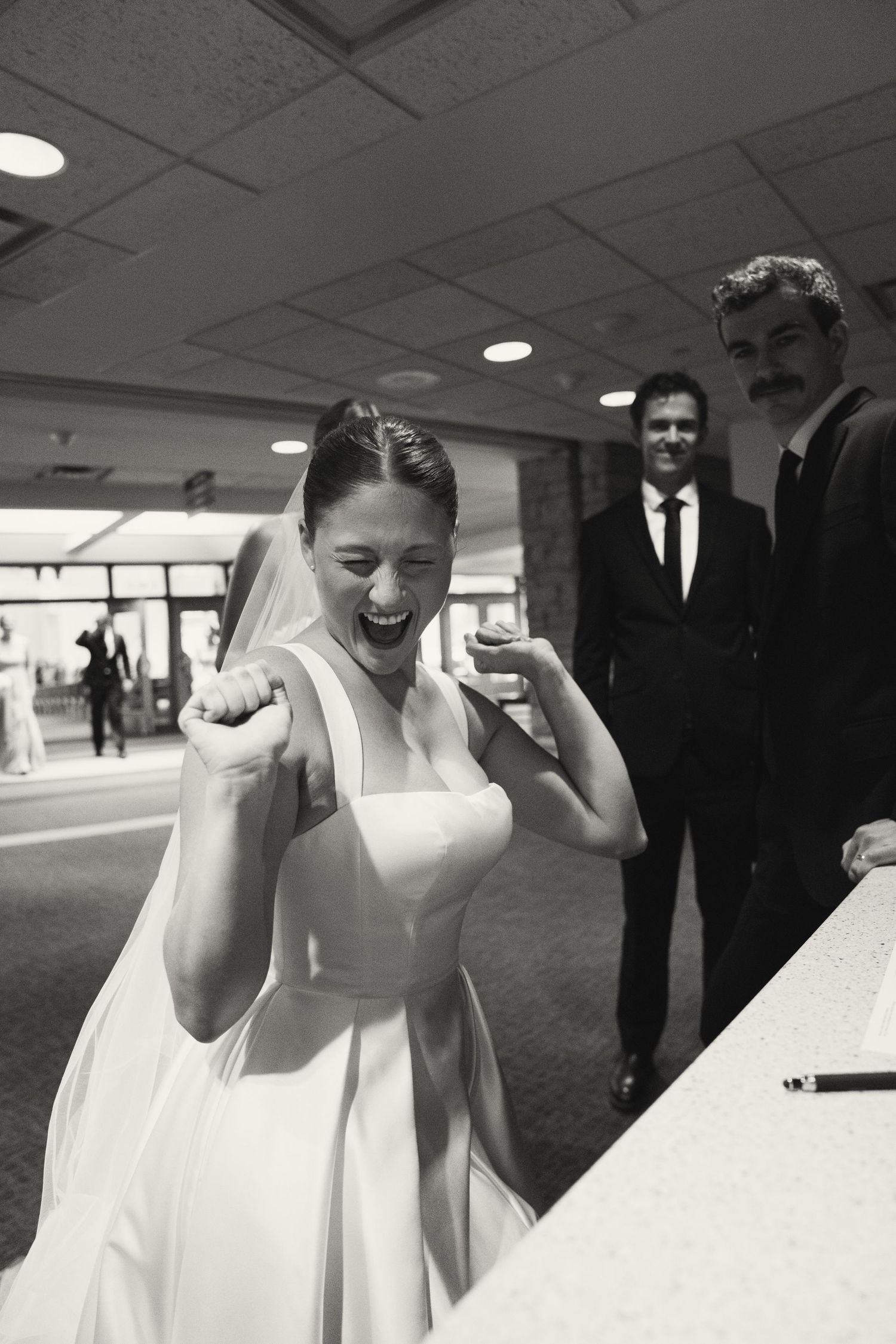 Bride in white dress celebrating joyfully in an indoor venue.