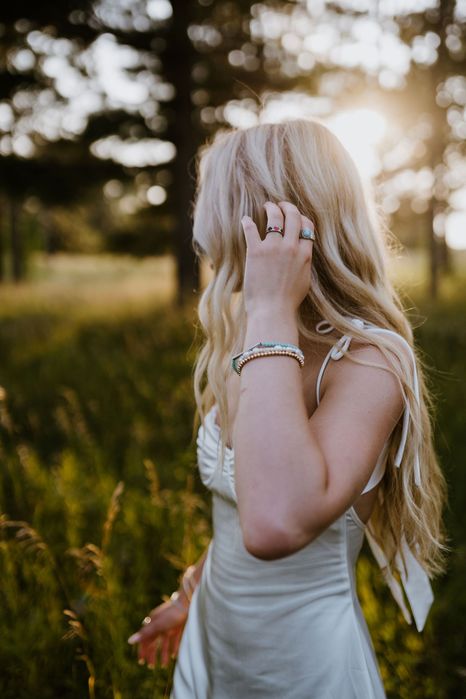 Close-up of hand with jewelry against sunset in summer field.