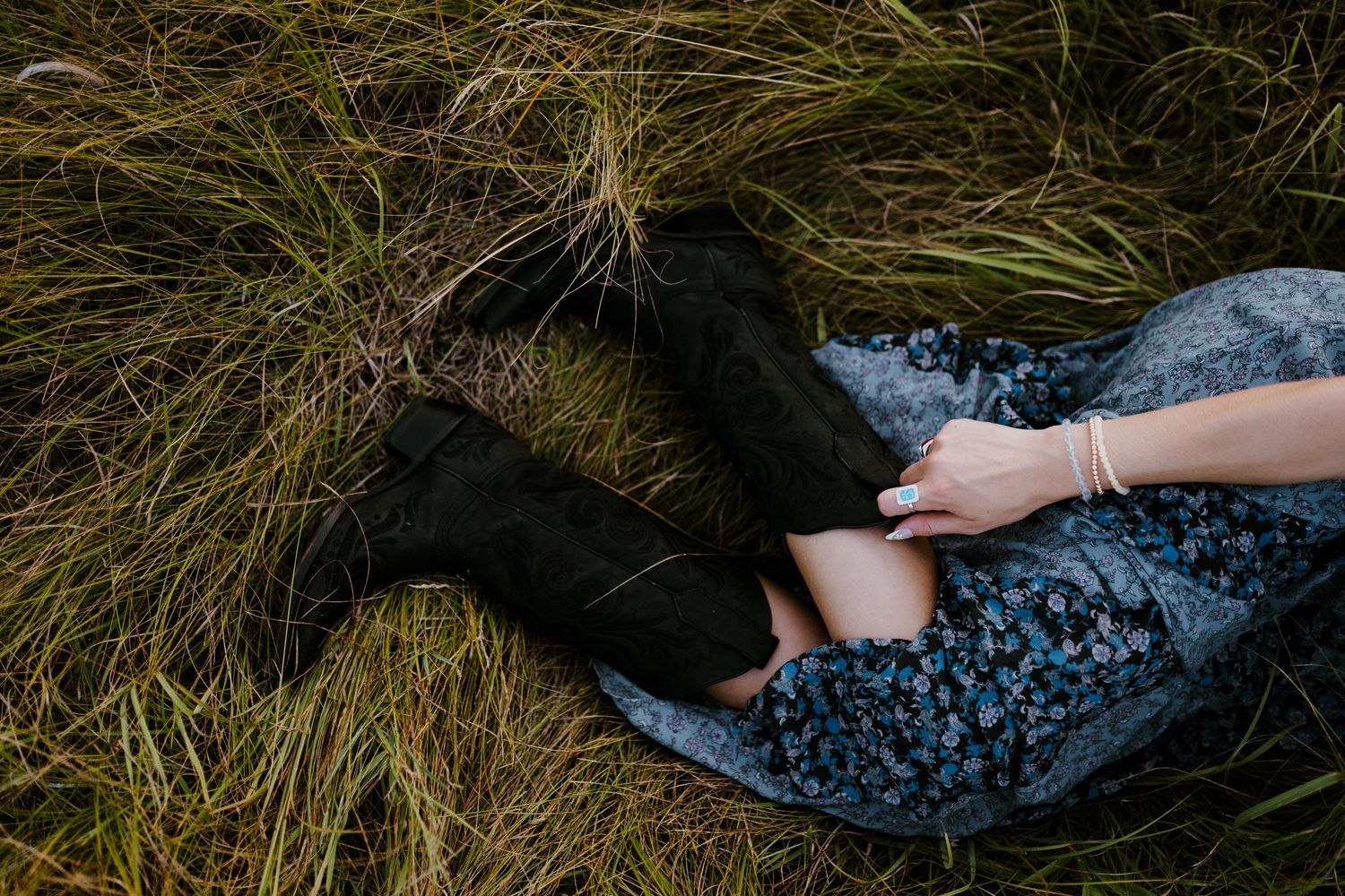 Person in floral dress and black boots lying in tall grass.