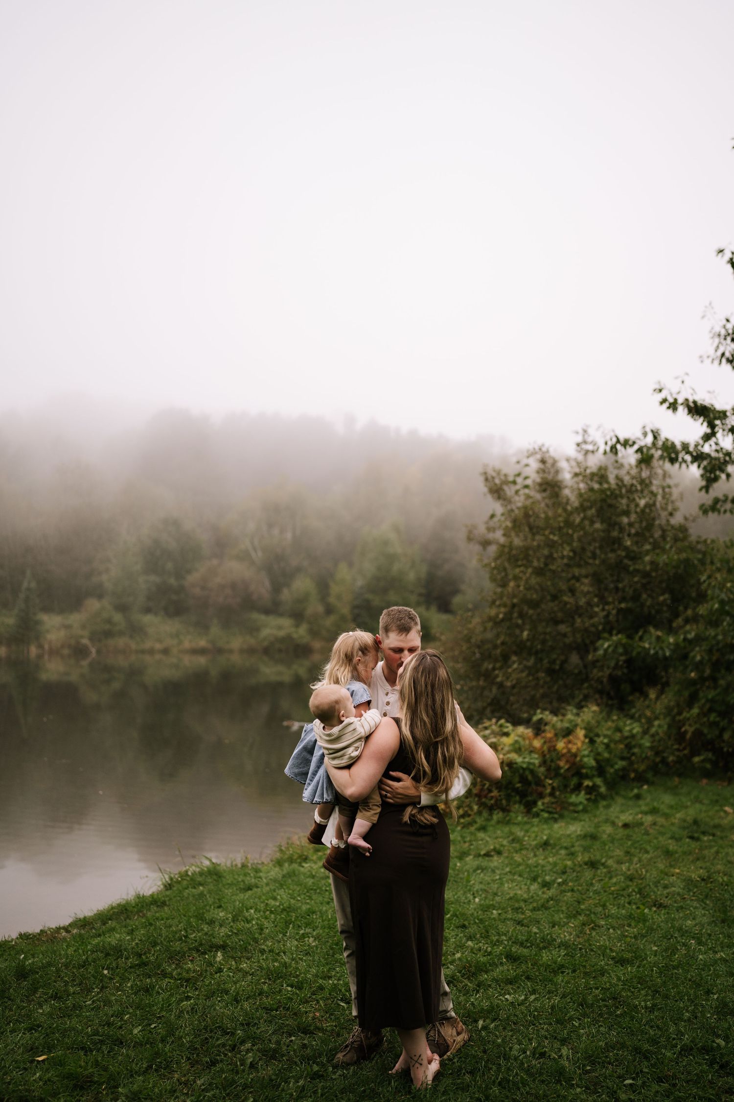 A tender family moment captured on a foggy lakeside hill.