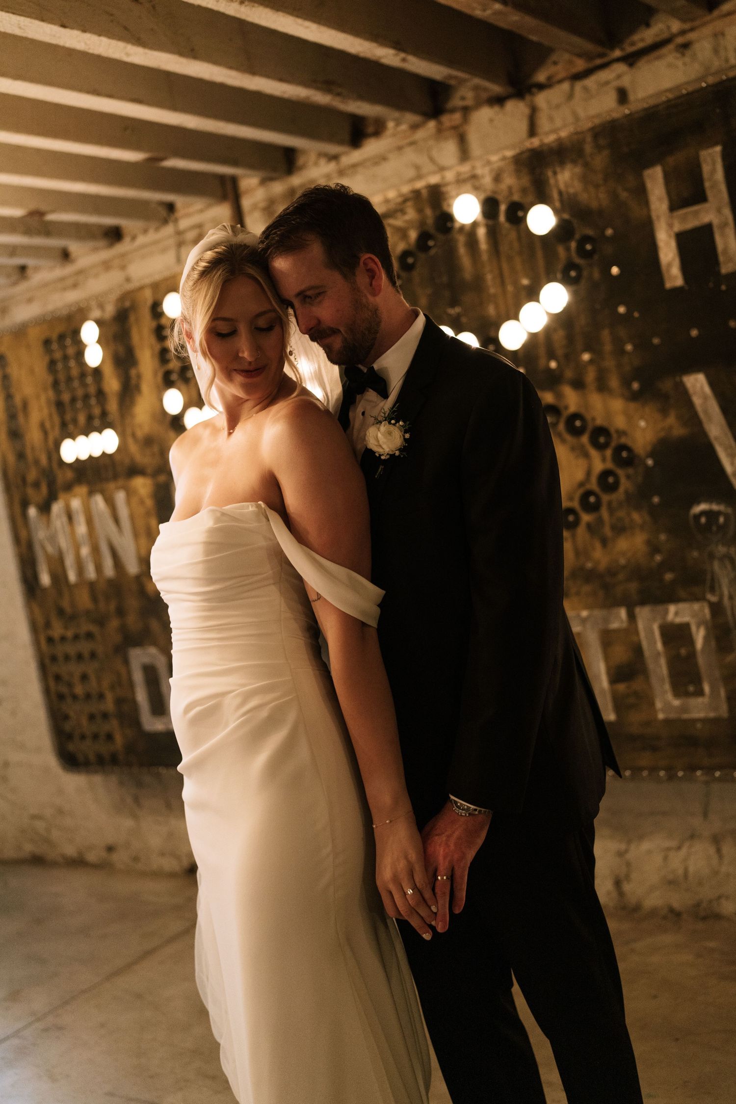 Couple shares intimate moment in rustic venue with exposed beams and string lights.