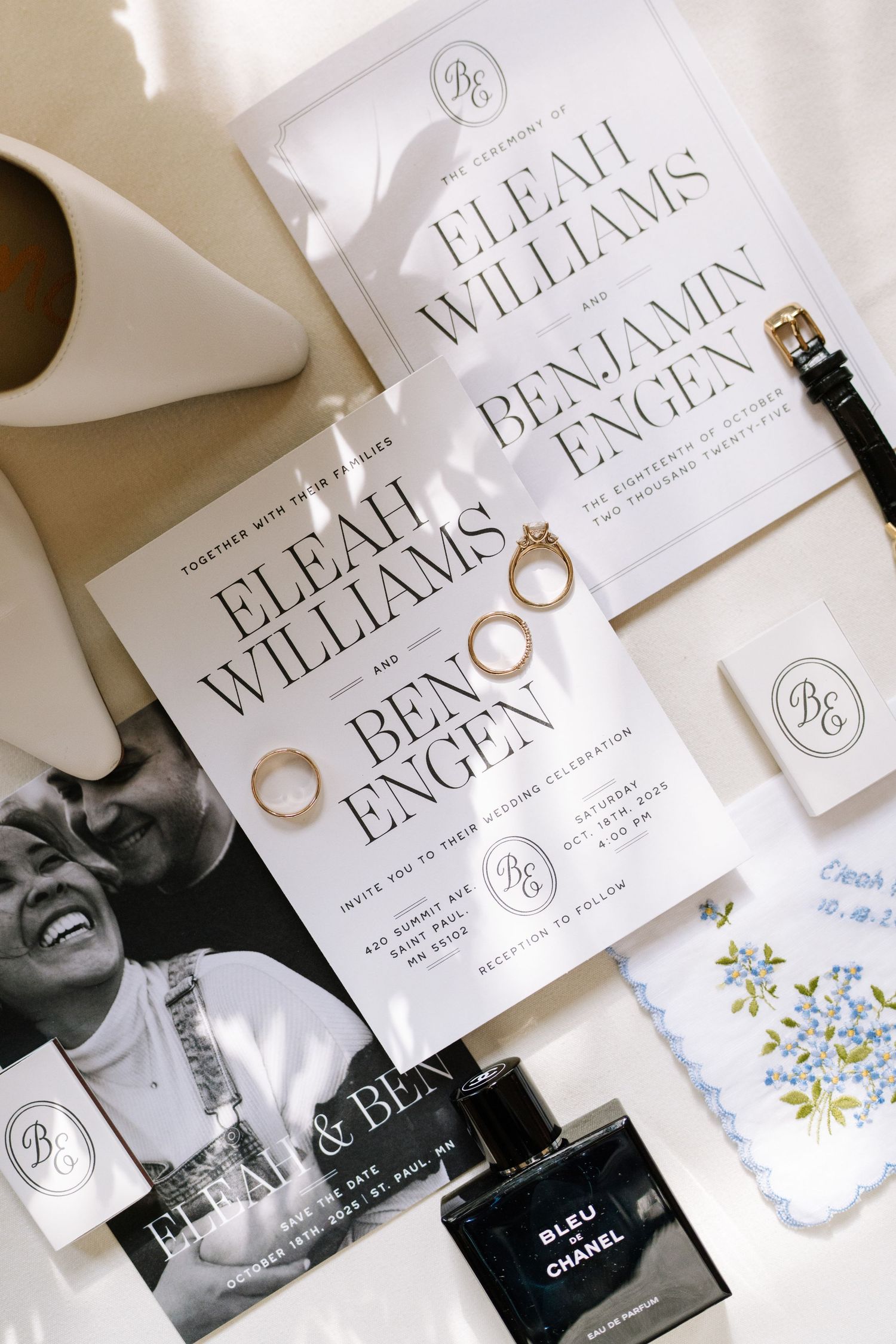 Elegant wedding invitations and perfume bottles arranged with rings on white surface.