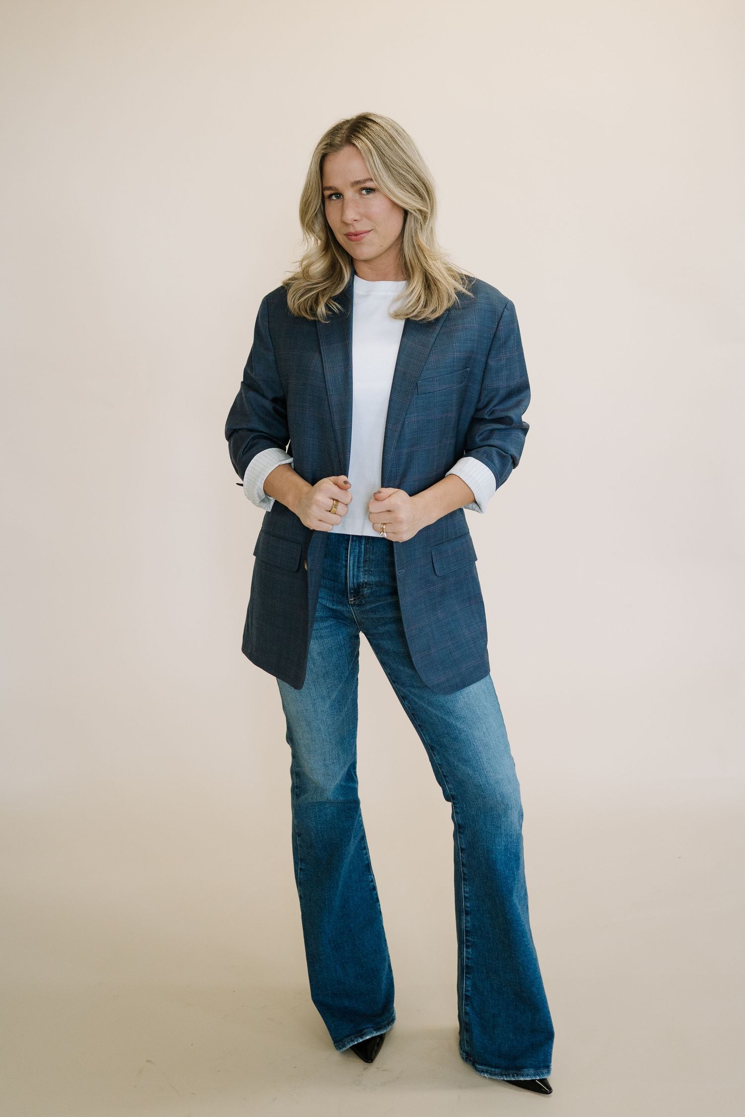 Business casual outfit with navy blazer and flared jeans against neutral background.