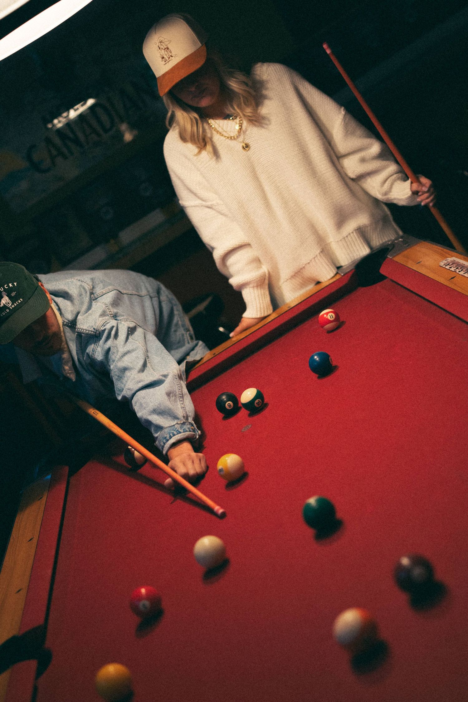 People playing pool on red felt table in dimly lit room.