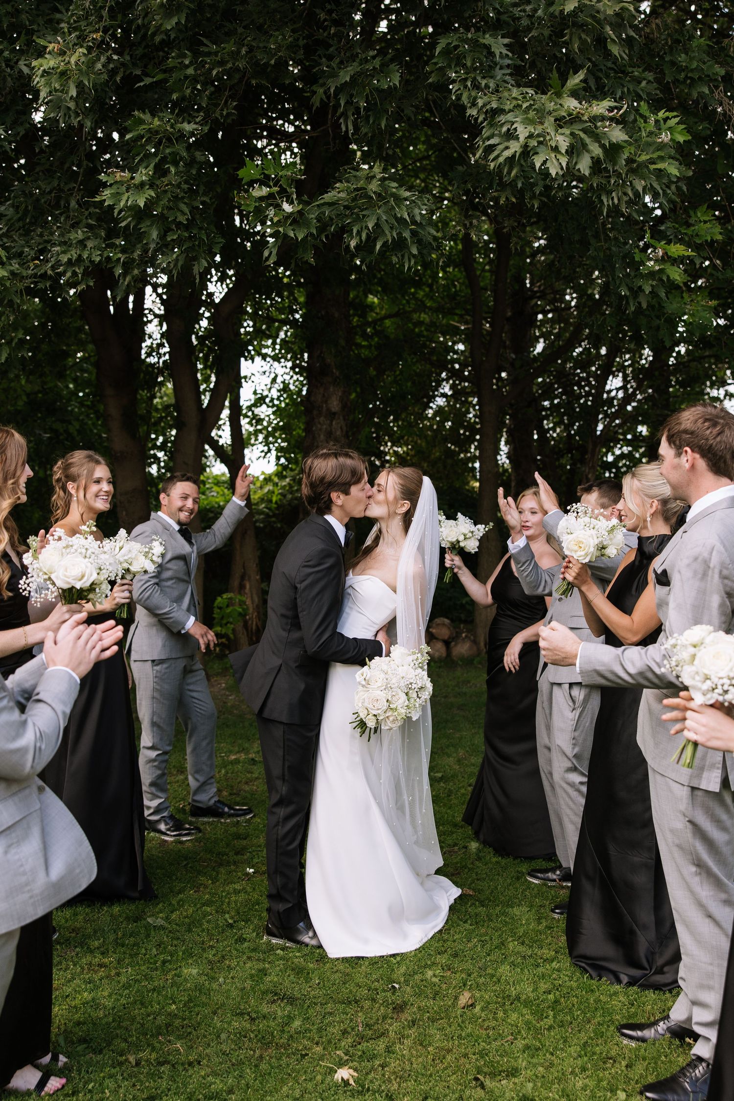 Large wedding party lined up outdoors celebrating with joyful expressions.