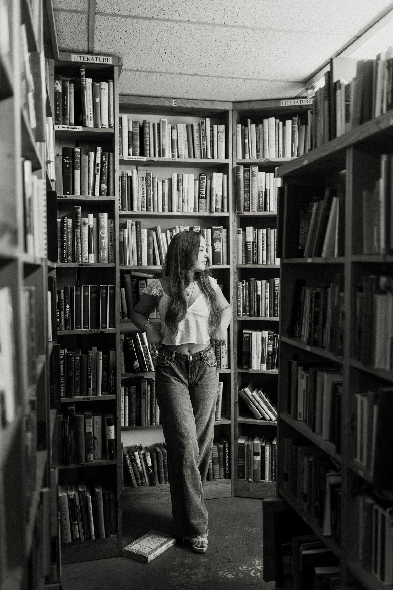 Monochrome image of someone exploring library stacks surrounded by books.