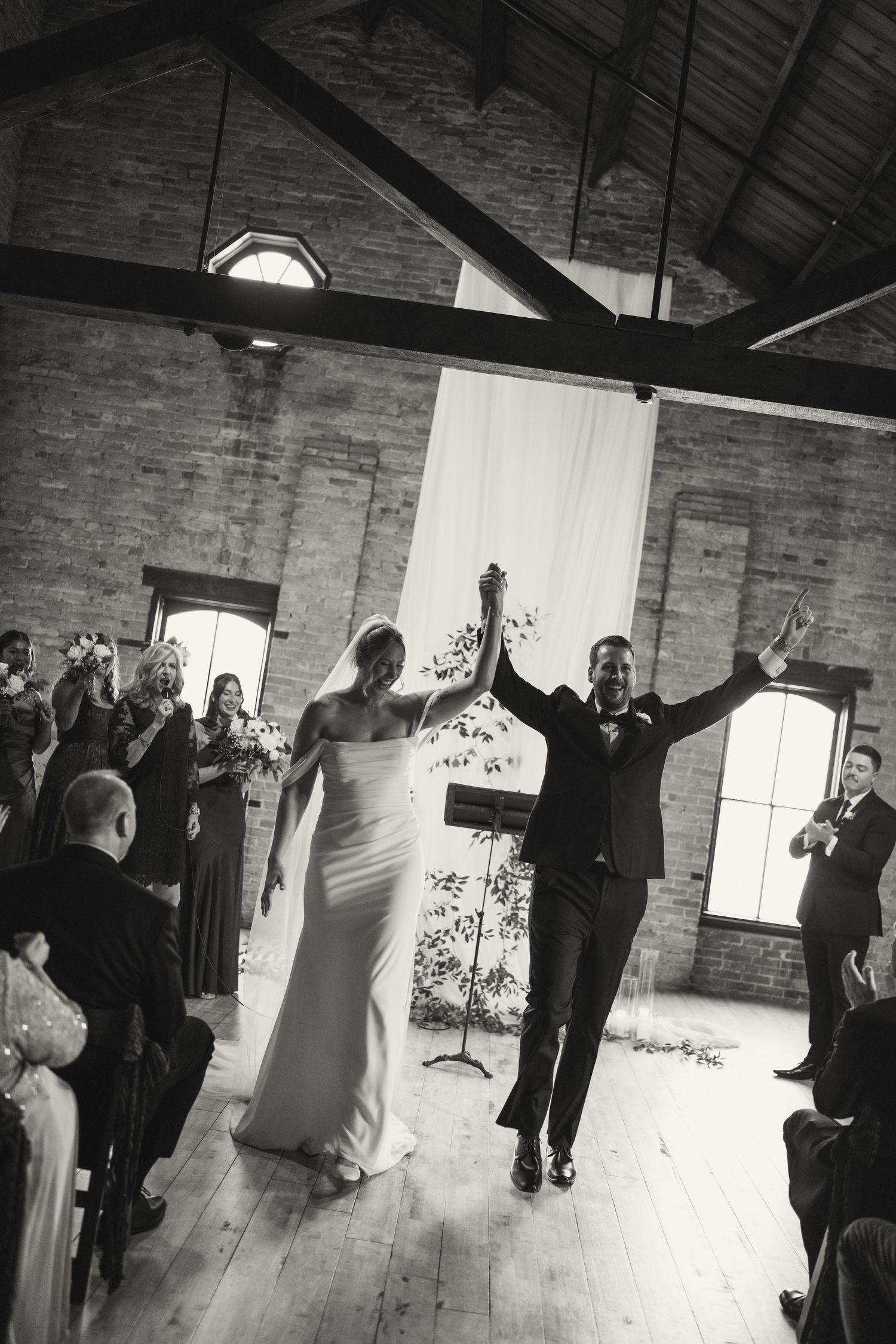 Wedding guests dance together in a rustic brick-walled venue during a celebration.