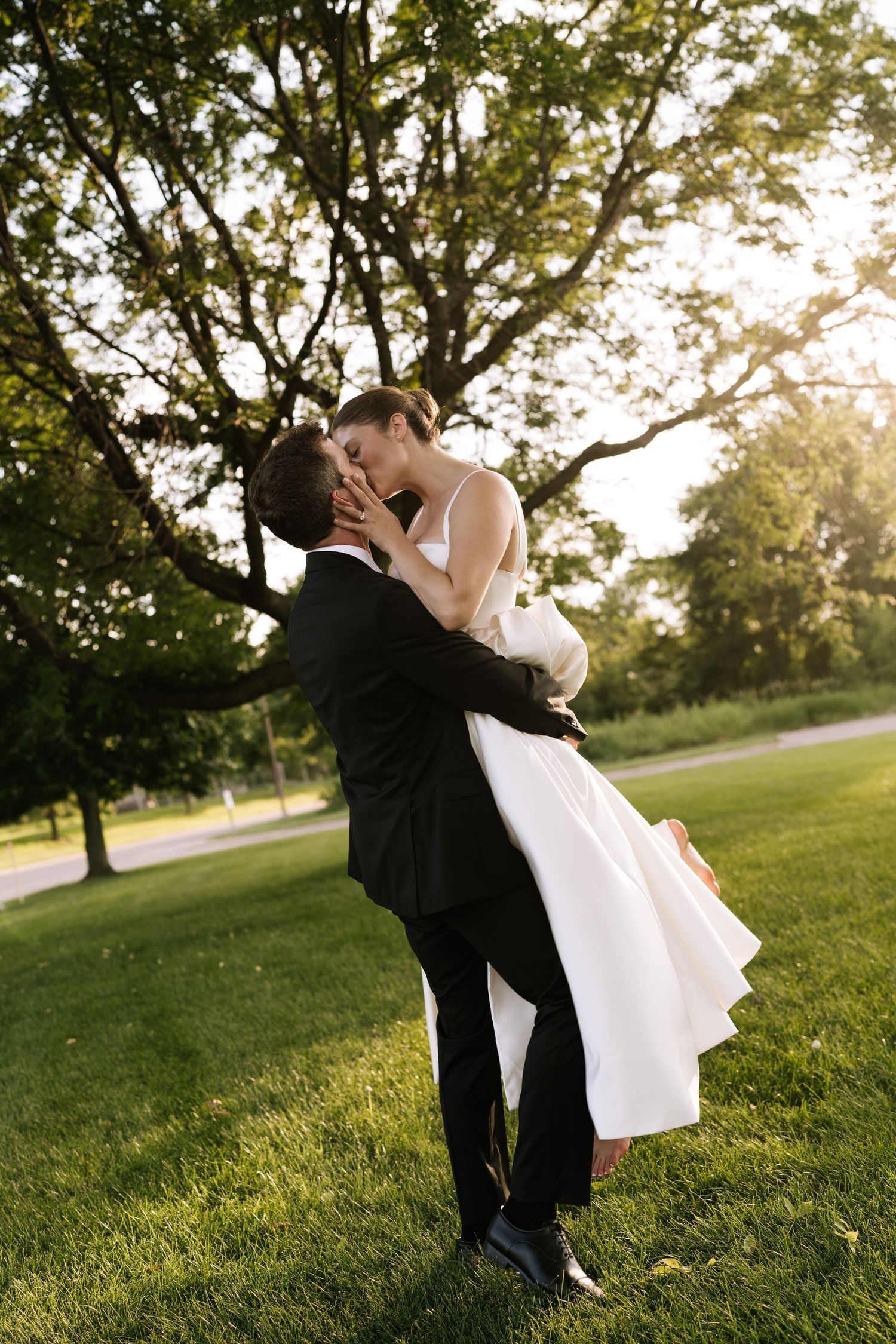Romantic wedding couple embracing in a sunlit garden setting with trees in the background.