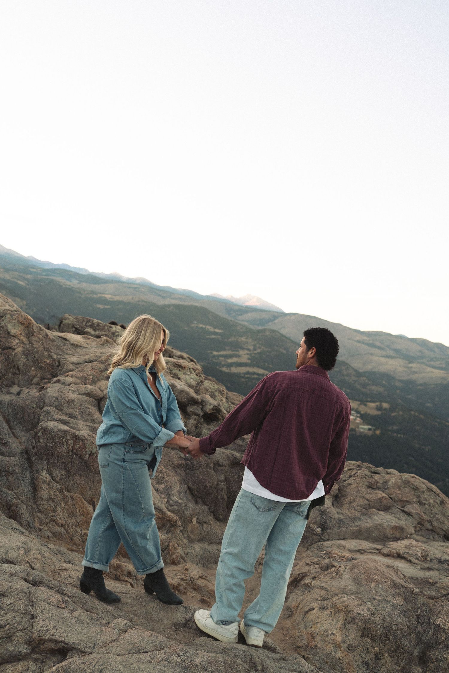 Two people playfully interact on rocky mountain terrain at sunset.