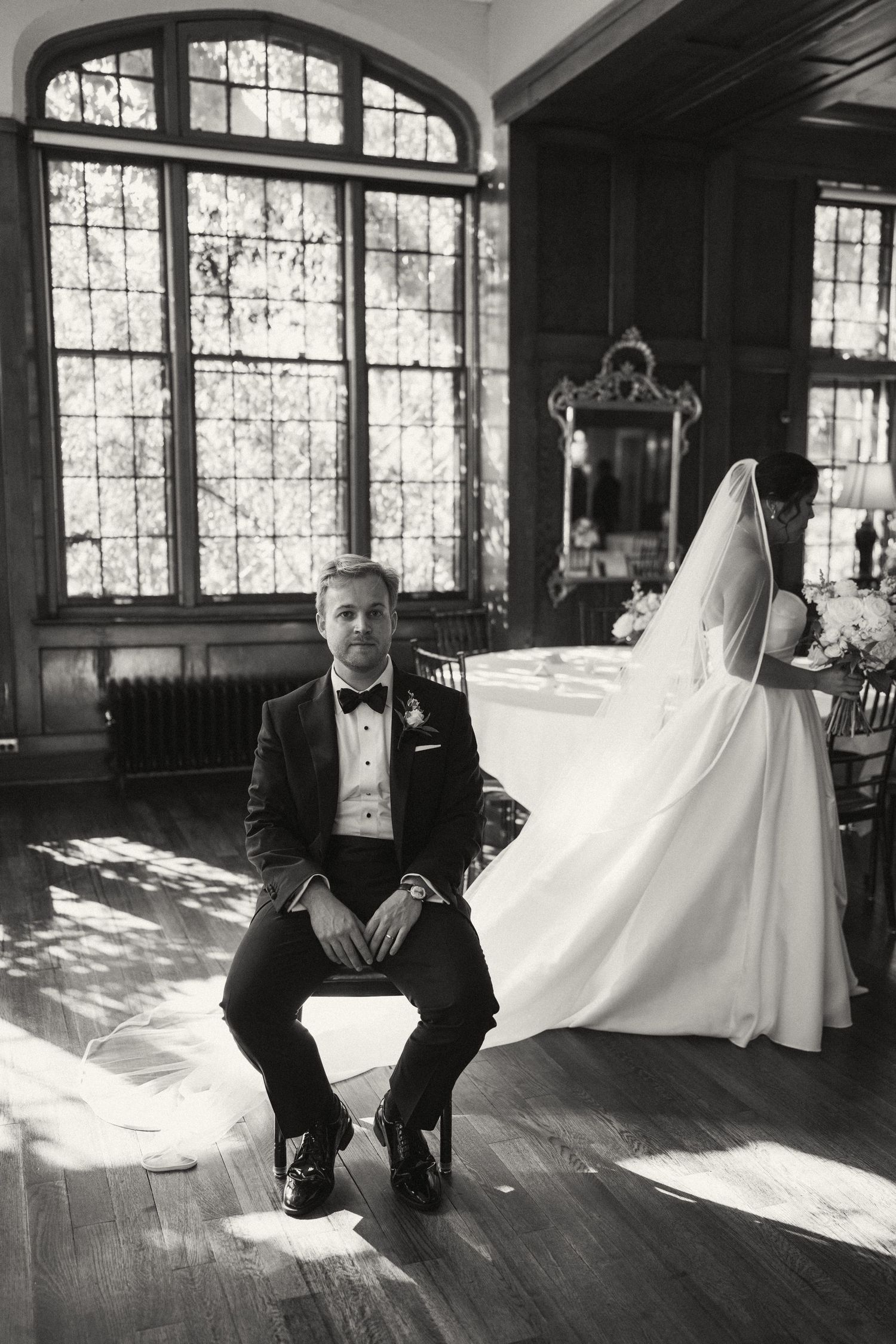 Black and white wedding photo with dramatic window light in an elegant indoor setting.