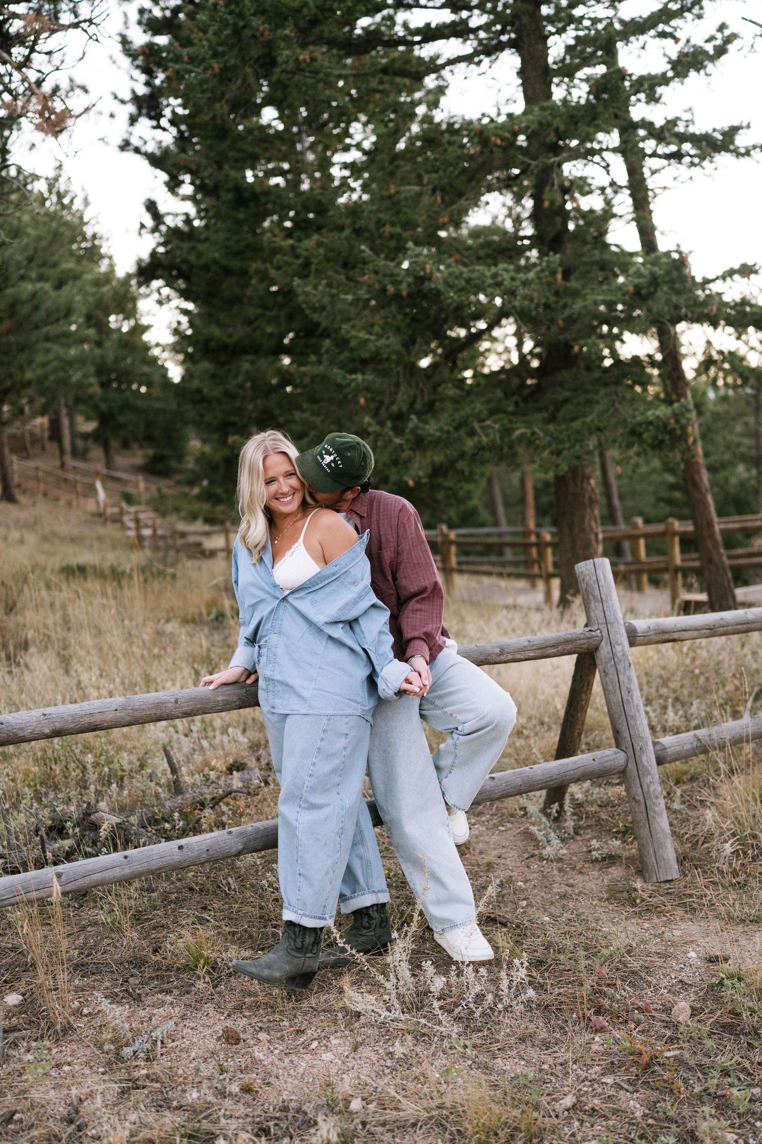 Couple shares romantic moments by rustic wooden fence in mountain setting.