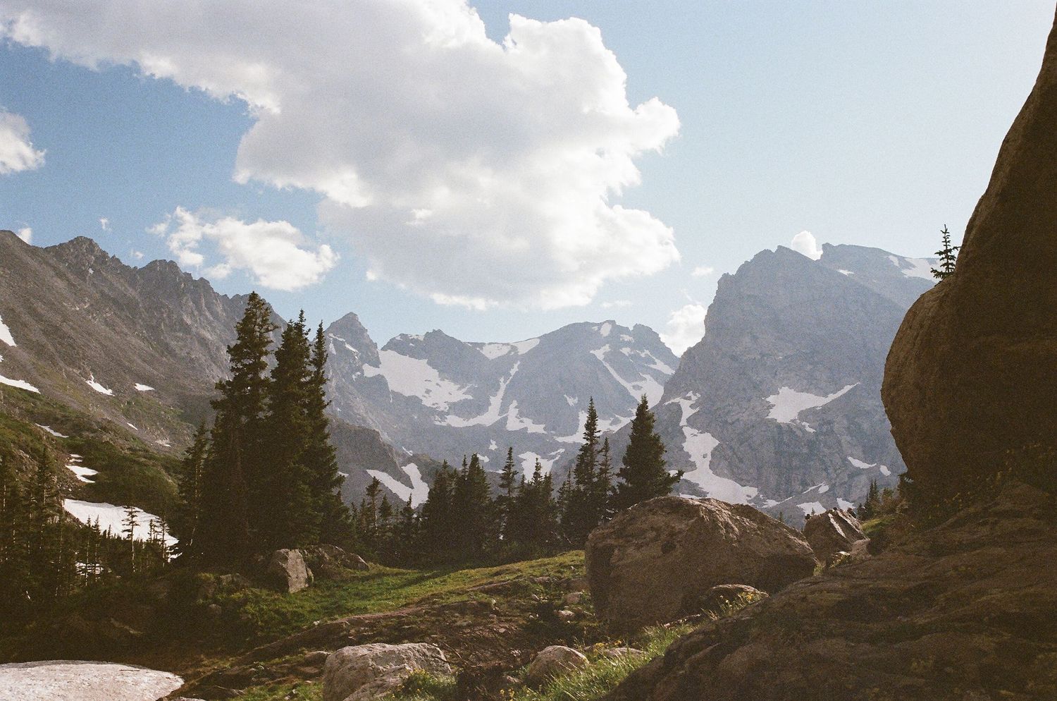 Panoramic view of snow-capped mountain peaks under a cloudy blue sky.