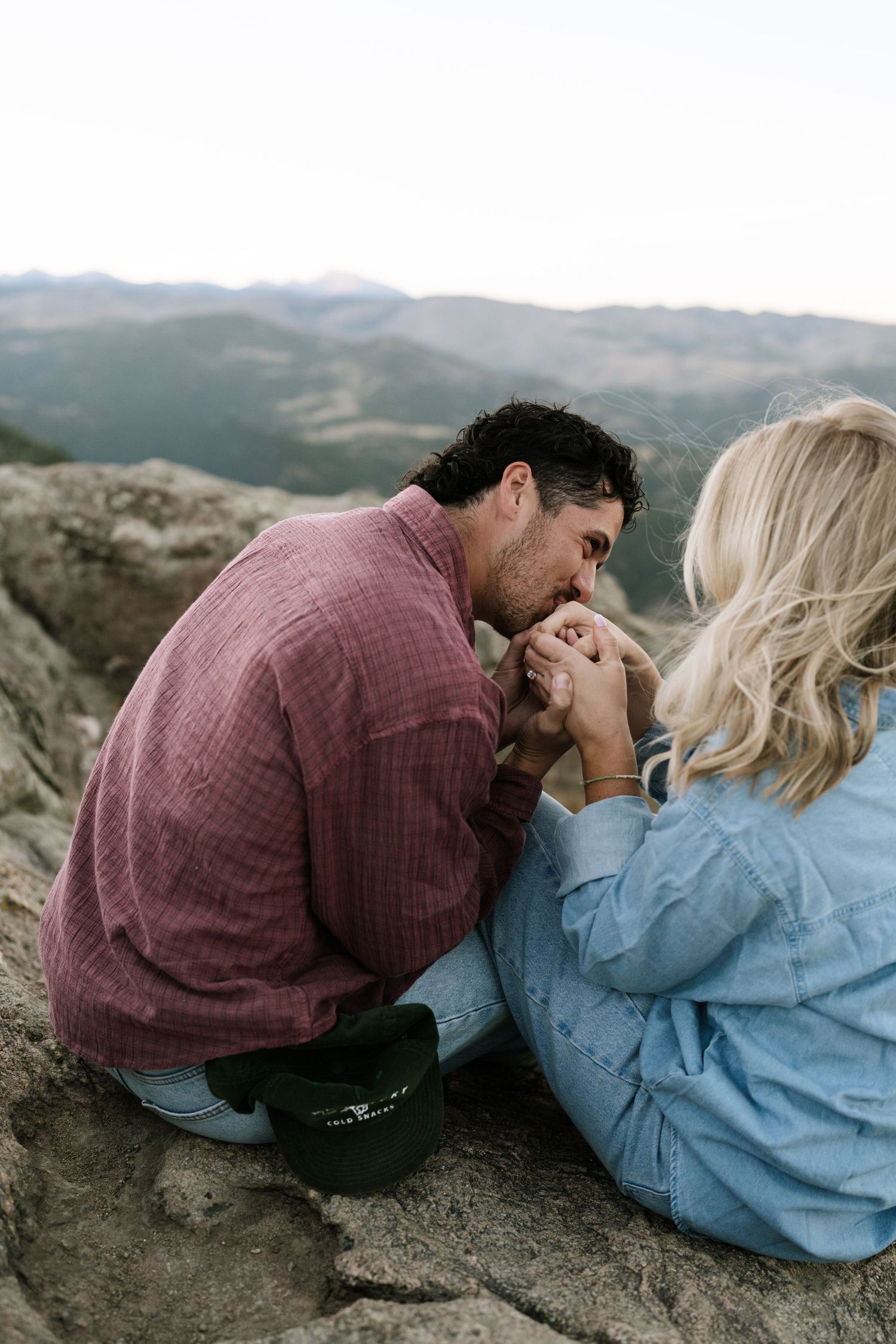 A couple shares an intimate moment lying on rocky terrain with mountains in the background.
