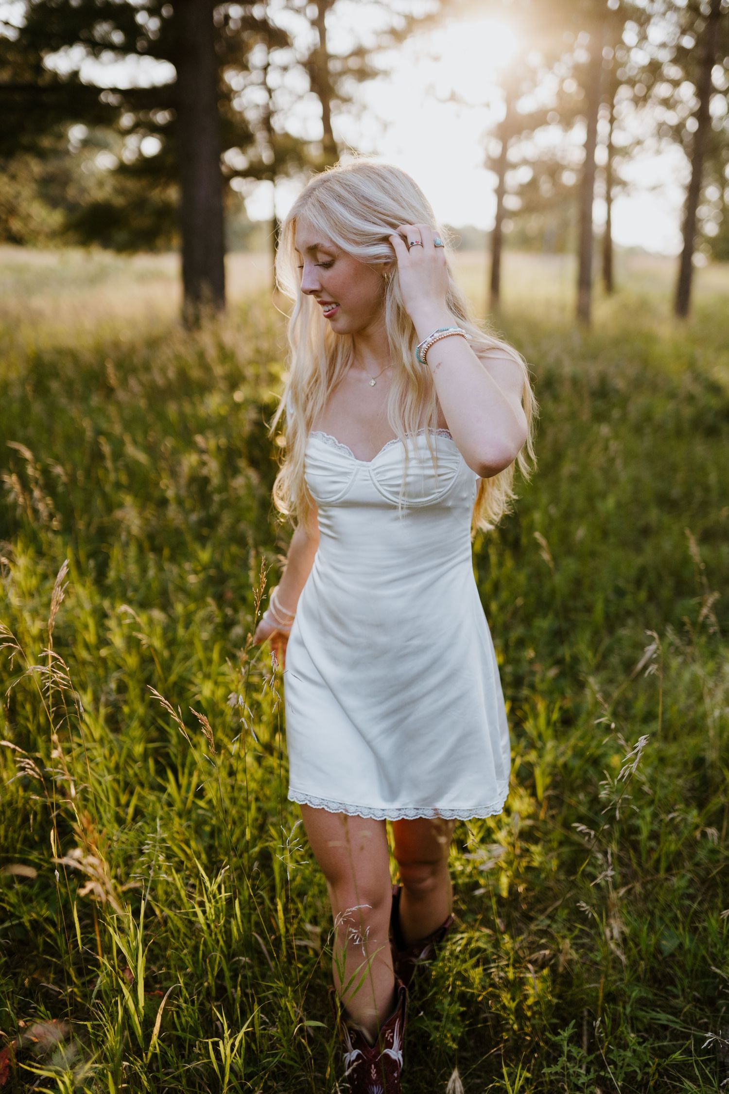 Person in white sundress and boots standing in sunlit meadow during golden hour.