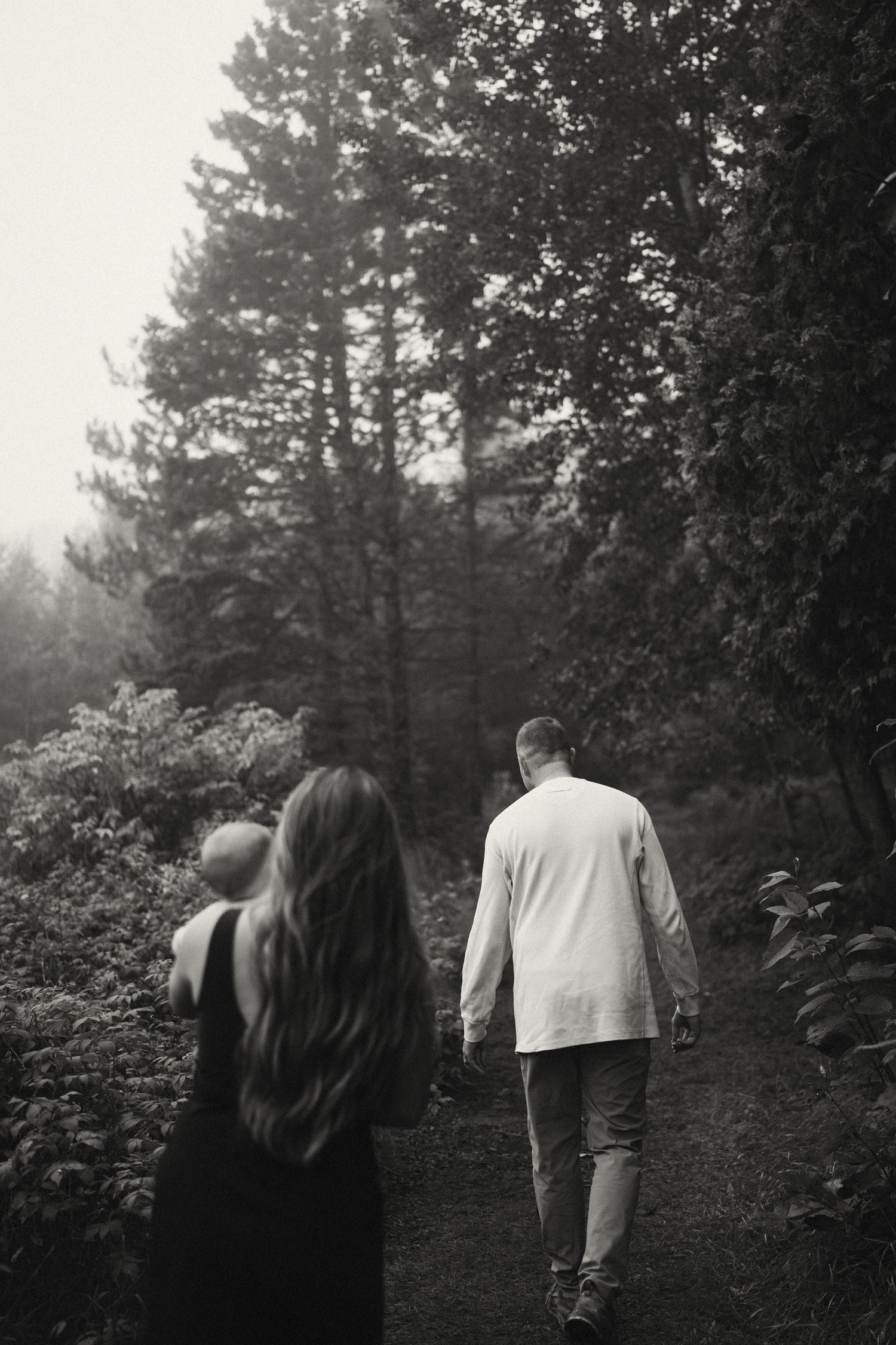 A moody black and white photo of people walking through a wooded path.