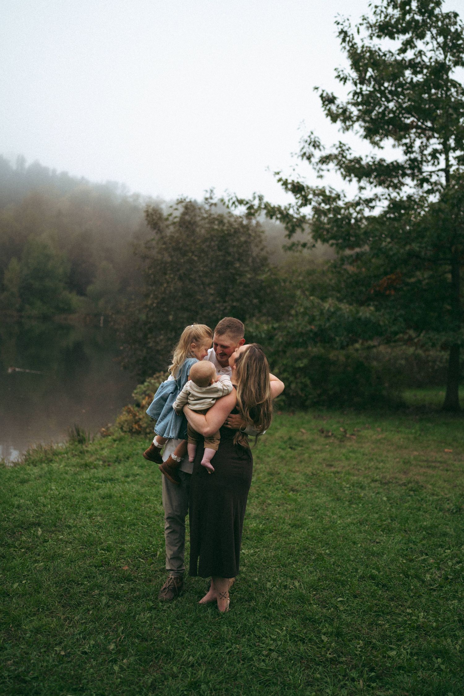 A family embraces together on a misty hillside with trees in the background.