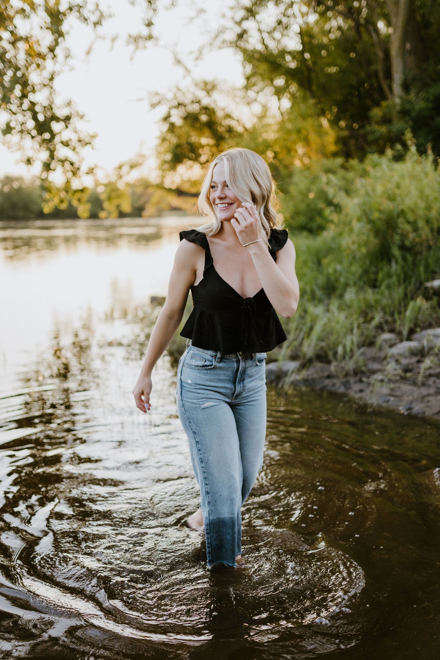 Someone walking through shallow water at sunset wearing jeans and a tank top.
