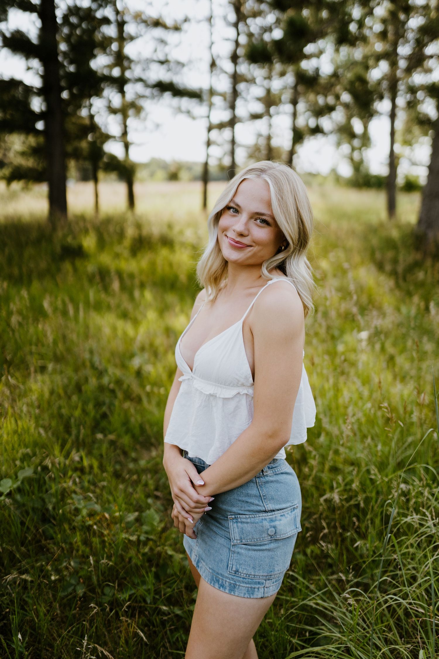 Summer portrait session in a grassy field features casual style with denim shorts and white top.