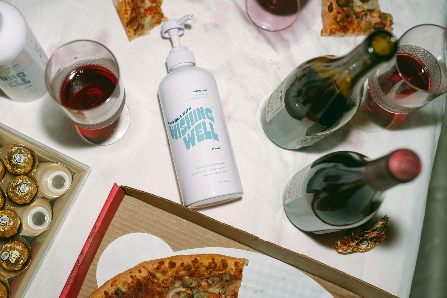 Overhead view of a table spread with pizza, wine glasses and snacks at a social gathering.