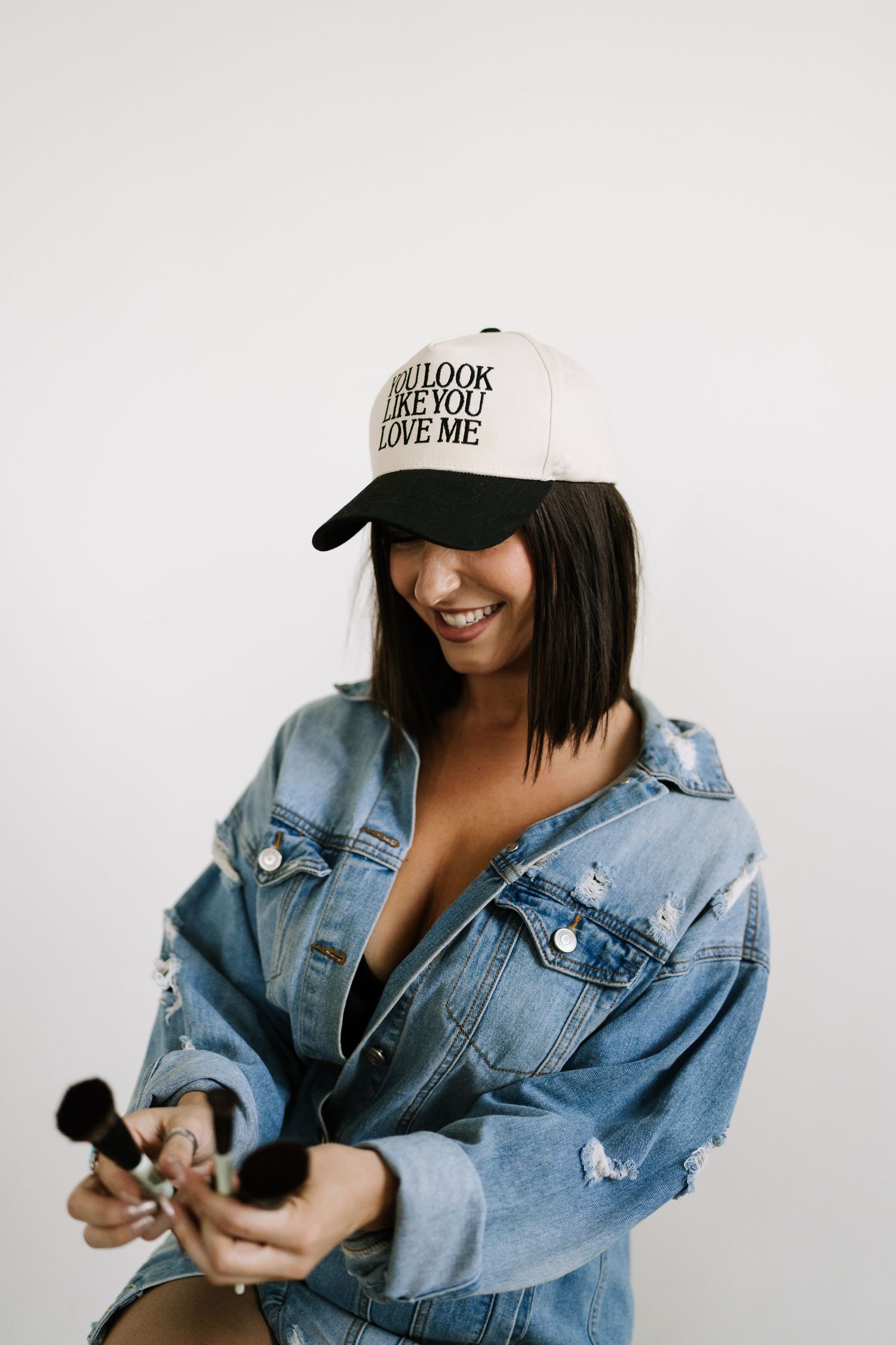 Casual portrait showing denim jacket and baseball cap with text against white background.