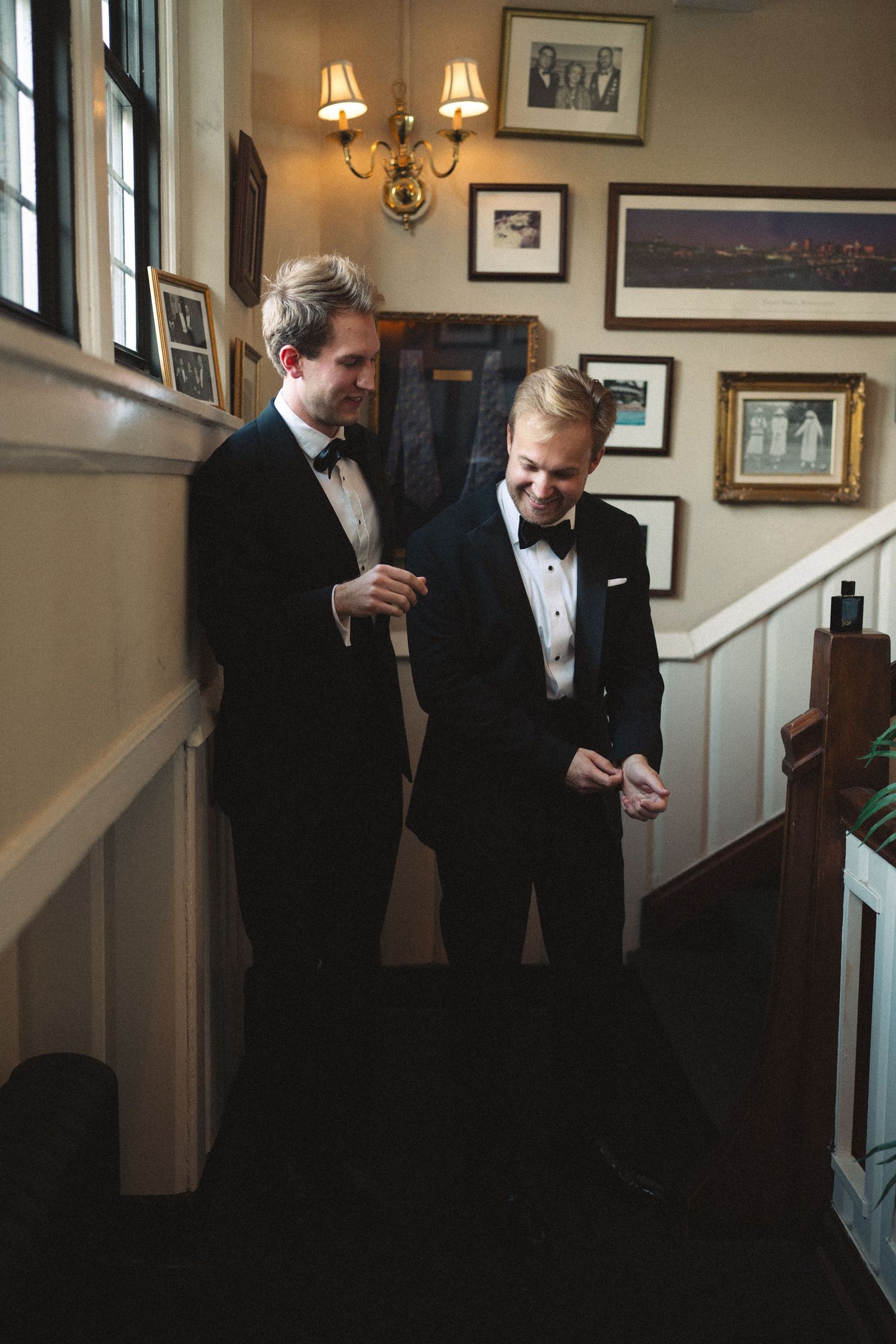 Groomsmen getting ready in formal attire in an elegant room with framed photos.