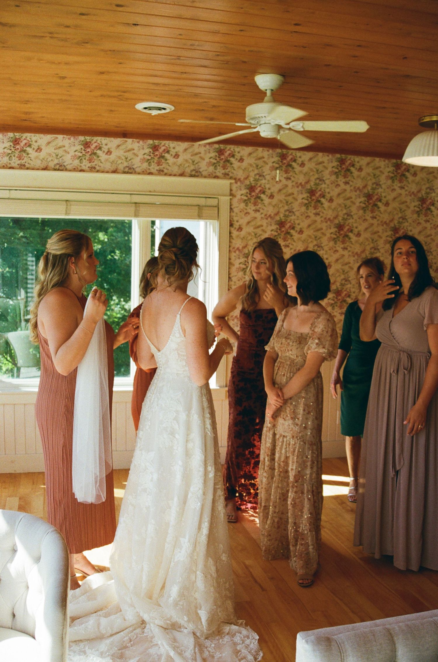 Wedding party getting ready in a rustic room with wooden floors and floral wallpaper.