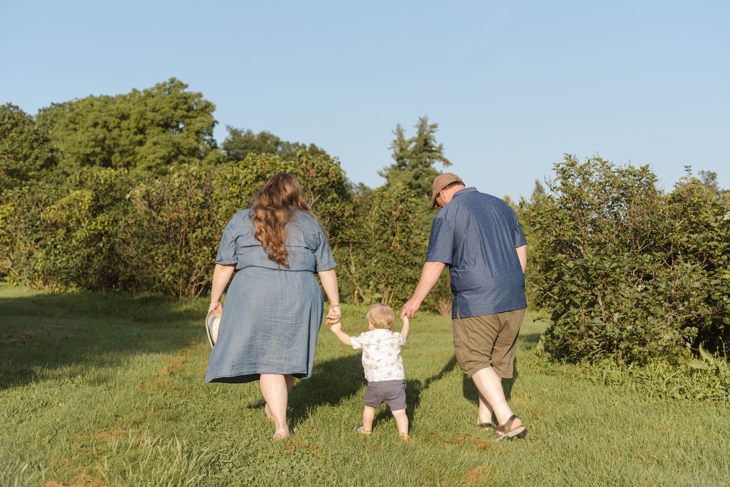 Family walking hand in hand with their young son during a photo session at Centennial Lilac Garden in Niagara Falls