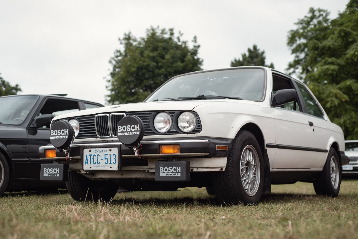 Front three-quarter view of a classic white BMW E30 with Bosch rally lights on display at TedFest in Niagara.