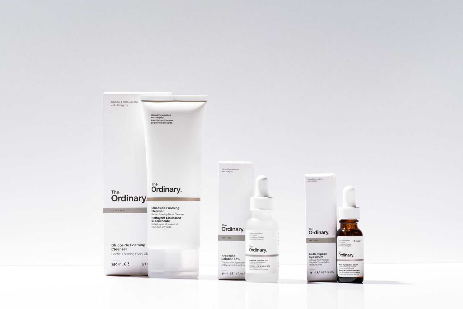 Studio product photography of The Ordinary skincare products, including cleanser and serums, styled on a clean white background.