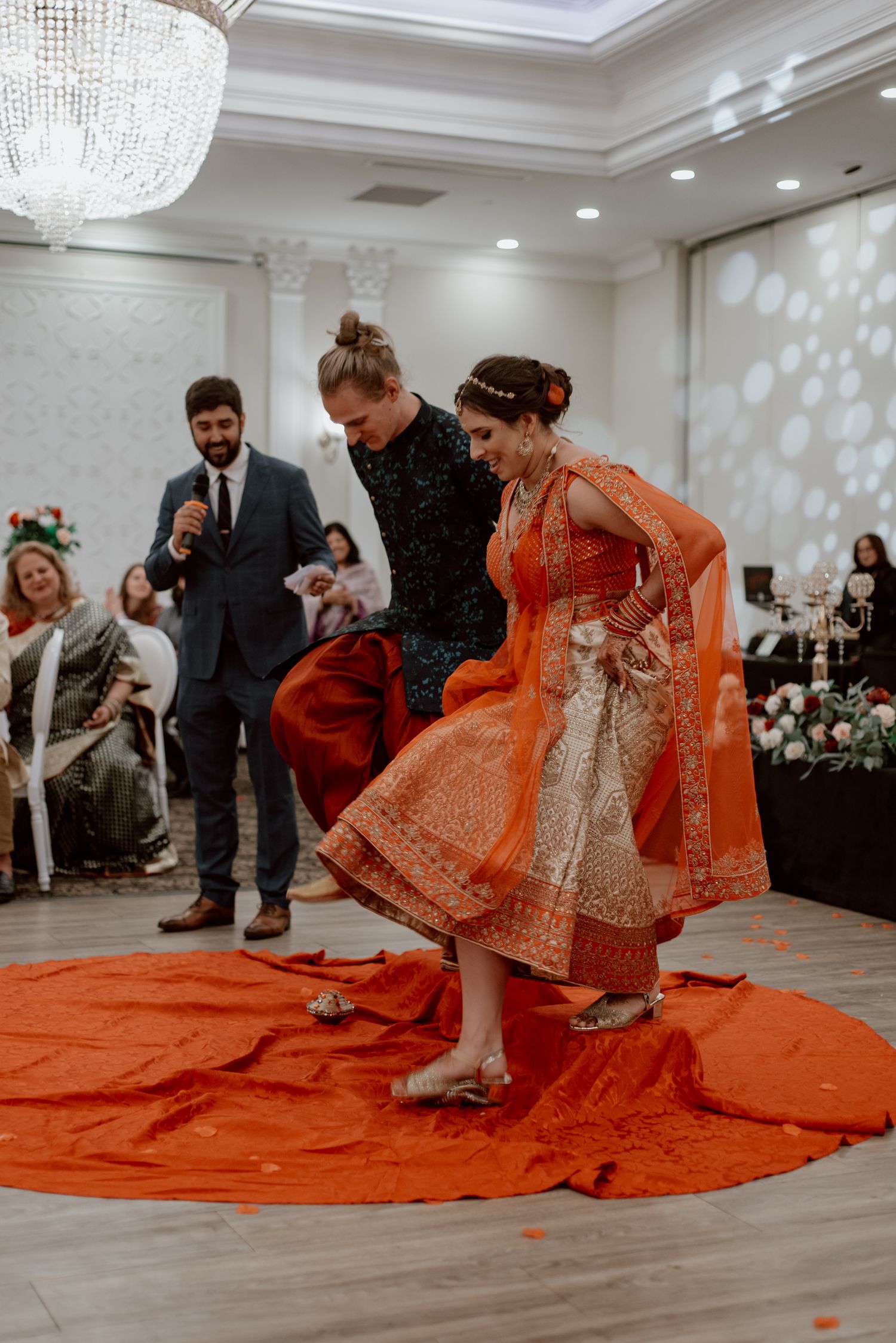 Candid wedding moment during a Mandvo ceremony, showing the couple stepping together in traditional attire at an indoor celebration.