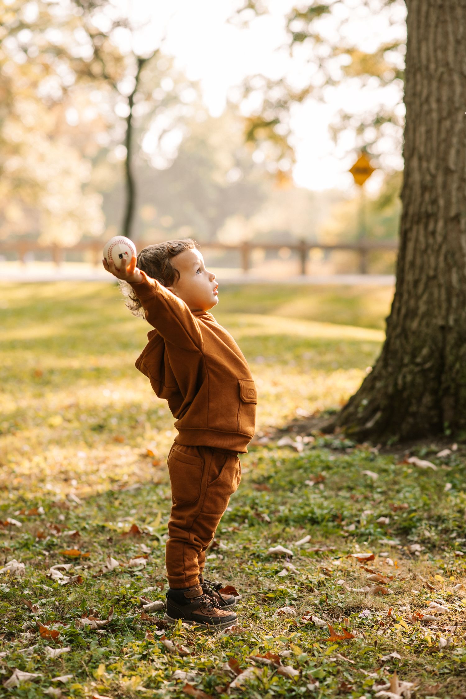 Candid family portrait of a toddler holding a ball in a park, captured outdoors in warm natural light during a fall photoshoot.