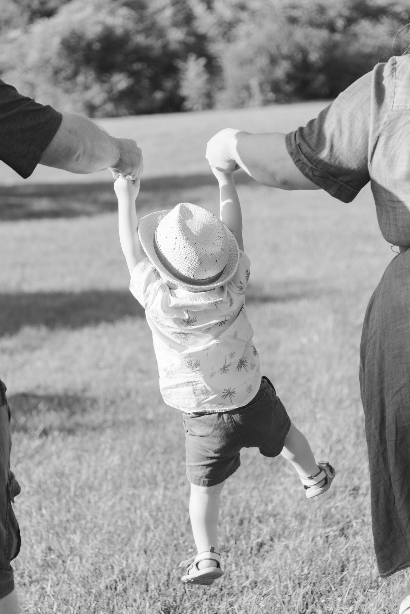 Black and white candid photo of a young boy swinging between his parents’ hands during a Niagara Falls family session