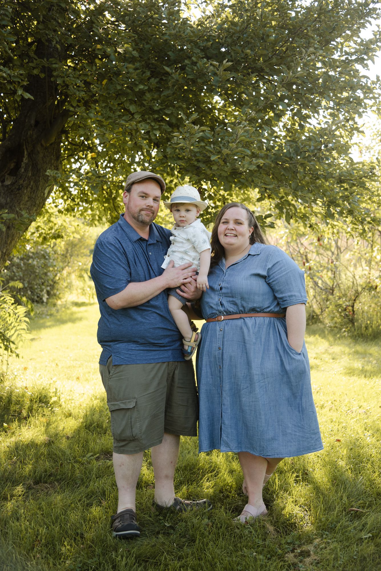 Family of three standing together under the trees during family photos at Centennial Lilac Garden in Niagara Falls