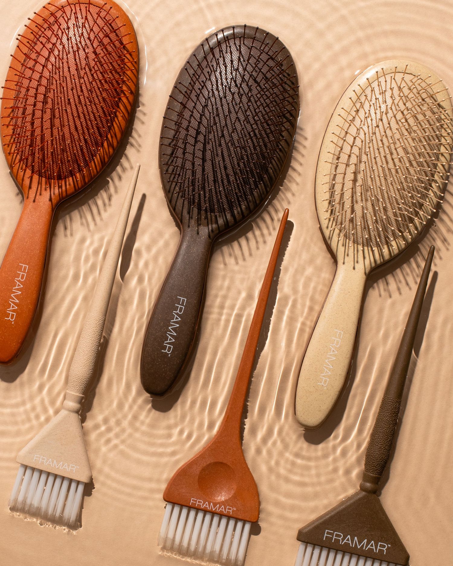 Studio product photography hair brushes and color tools in warm, earthy tones styled with water and natural light.