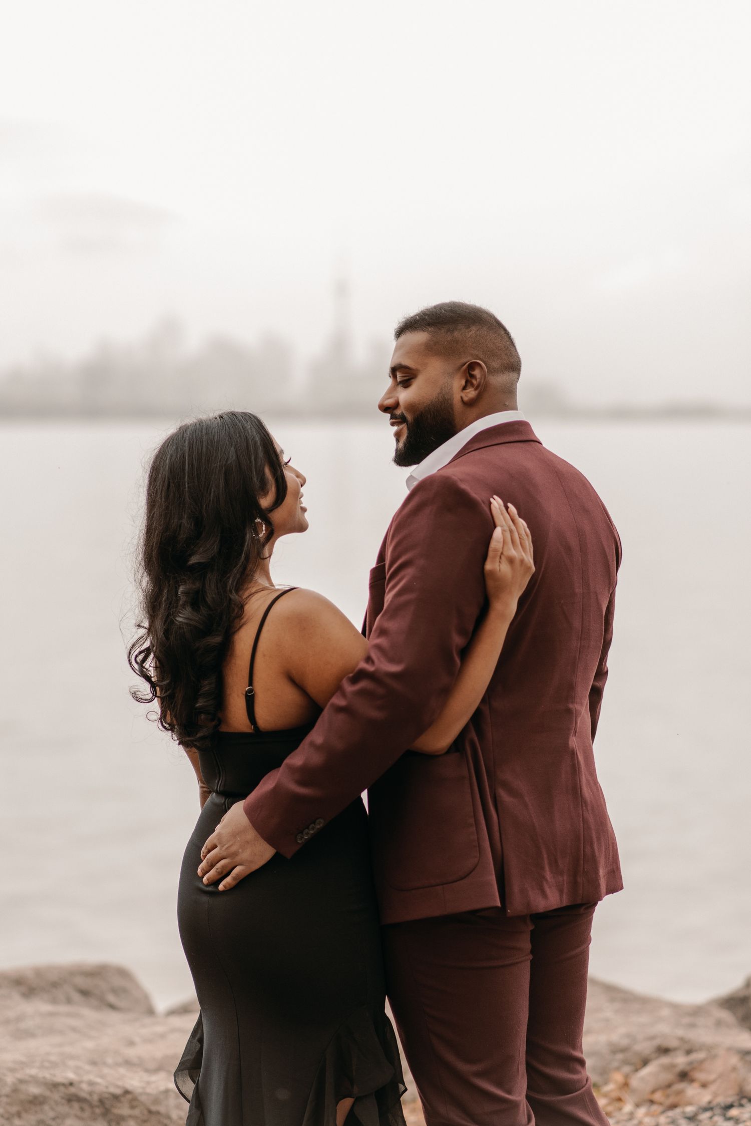Engagement portrait of a couple embracing by the water, sharing a quiet, intimate moment during a proposal photoshoot.