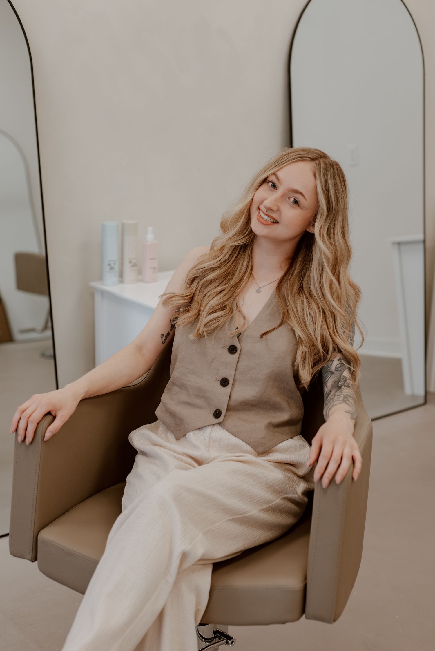 Branding portrait of a hairstylist seated in a studio chair, smiling in a neutral-toned space designed for Instagram-ready content.